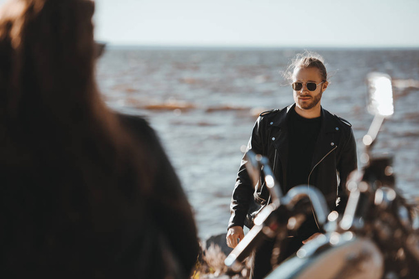 selective focus of female biker sitting on motorcycle and looking at man walking on seashore  - Fotó, kép
