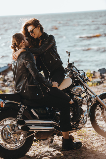 couple of bikers hugging on classical motorcycle on seashore - Photo, Image