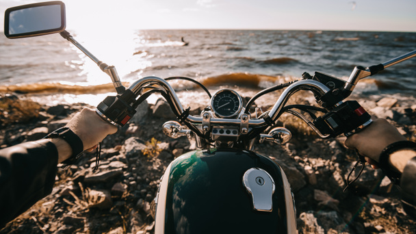 Camera point of view of biker sitting on classic motorbike on seashore - Фото, зображення