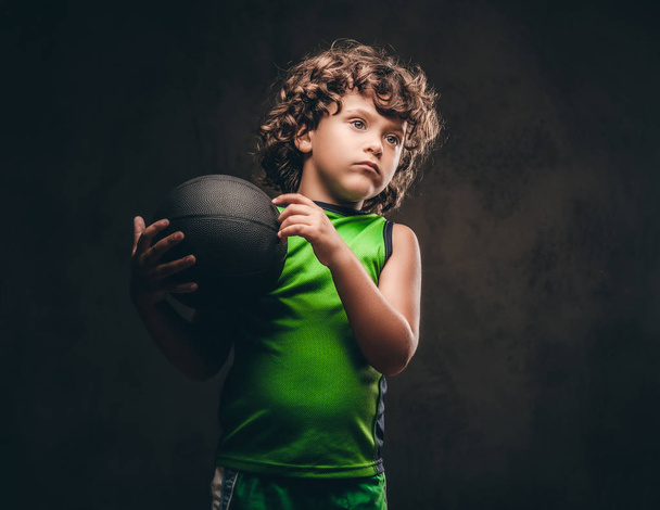 スタジオでボールを保持しているスポーツウェアの小さなバスケット ボール選手。ダーク テクスチャ背景に分離. - 写真・画像