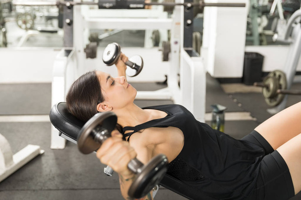 Side view of female client doing dumbbell fly on bench in gym - Fotoğraf, Görsel