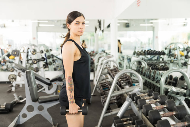 Φίλαθλη αθλητική γυναίκα με αλτήρες στέκεται μπροστά από καθρέφτη στο γυμναστήριο - Φωτογραφία, εικόνα