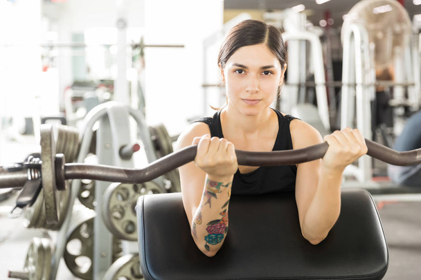 Retrato de atleta femenina confiada levantando rizos de barra en la máquina de ejercicio en el gimnasio
 - Foto, imagen