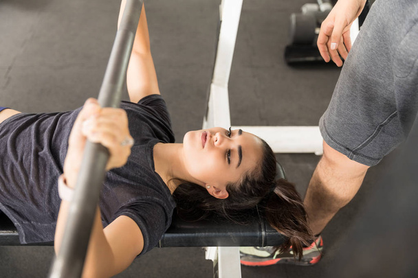Young sporty woman doing the bench press by instructor in gym - Photo, Image