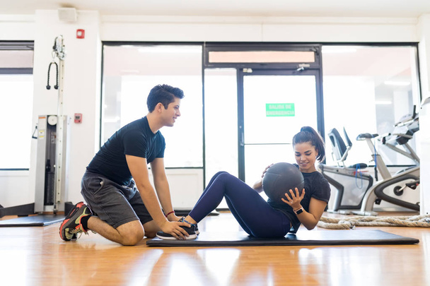 Kadın sağlık topu içinde jimnastik salonu ile karın egzersiz yaparken yardımcı genç erkek eğitmen - Fotoğraf, Görsel