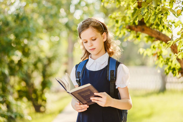 cute schoolgirl reads book outdoors - Fotó, kép