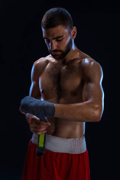 Sportboxermann zieht an der Handgelenksbandage. orientalische männliche Modell isoliert auf schwarzem Hintergrund. - Foto, Bild