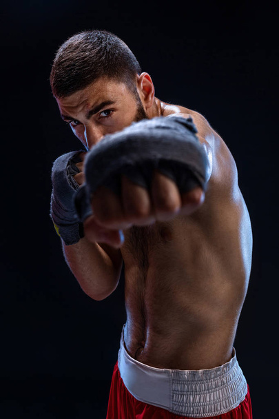 El boxeador está listo para dar un golpe poderoso. Foto de un hombre musculoso con manos fuertes y puños apretados en rayas azules sobre fondo negro
. - Foto, Imagen