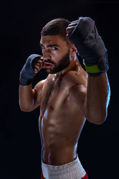 Boxing man ready to fight. Boxer with strong hands and clenched fists in blue straps against a black background - Photo, Image