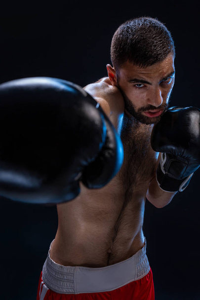 Portrait of tough male boxer posing in boxing stance against black background. - Photo, Image