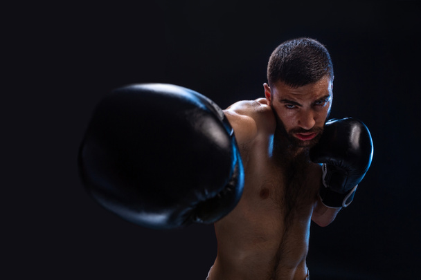 El hombre está golpeando a un oponente. Luchador enfocado con torso desnudo y guantes de boxeo mirando a la cámara. Ganar
. - Foto, Imagen
