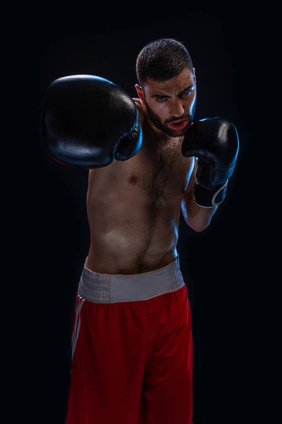El boxeador está listo para dar un golpe poderoso. Foto de hombre musculoso sobre fondo negro
. - Foto, Imagen