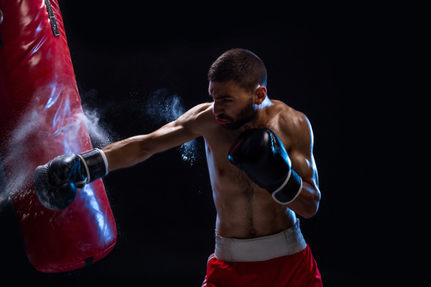 Entraînement de boxeur masculin barbu avec sac de boxe sur fond noir. boxeur masculin comme exercice pour le grand combat
. - Photo, image