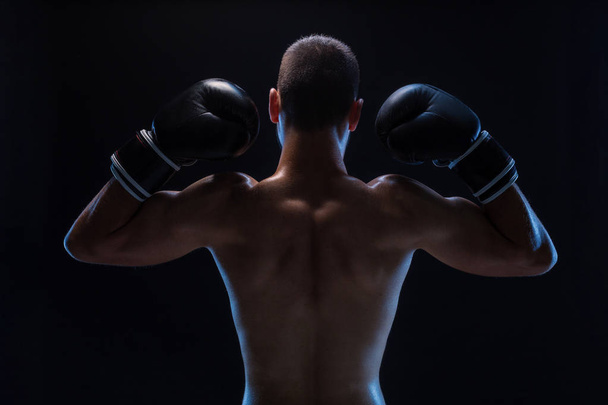 Widok z tyłu mocny młody mężczyzna boksera. Fitness model mężczyzna nosić rękawice bokserskie, stojąc na czarnym tle. - Zdjęcie, obraz