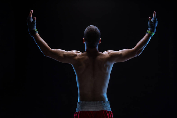 Rear view of strong young male boxer. Fitness male model wearing boxing gloves standing on black background. - Photo, Image