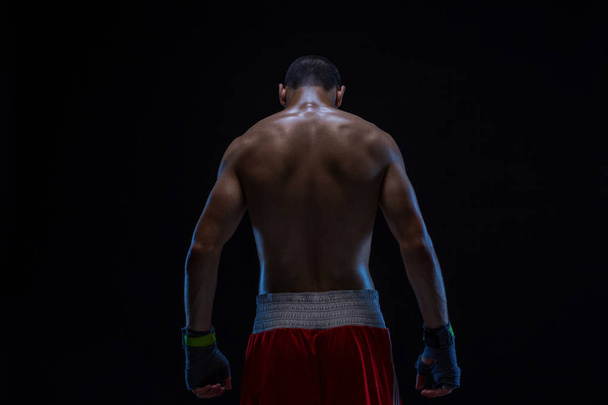 Nézet hátulról erős fiatal férfi boxer. Fitness férfi modell állandó fekete háttér, boksz-kesztyűket visel. - Fotó, kép