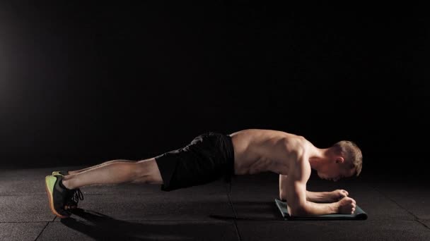 strong man is performing physical static exercise a plank, leaning by hands on floor, face down in a gymnastic hall - Materiaali, video
