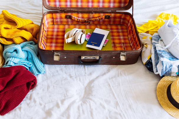 maleta con ropa de invierno y verano en la cama. preparándose para el viaje. maleta con prenda. concepto de viaje
 - Foto, Imagen
