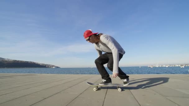 スローモーションを閉じる: スケート ボード、オリーをジャンプ若いプロのスケートボーダー フリップ トリック海岸沿いの遊歩道の日当たりの良い夏の。海の近くのスケート ボードとキックフ リップ トリック ジャンプのスケートボーダー - 映像、動画