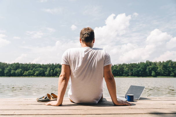 az ember ül a laptop, és a tóra néz. munka nyaralás. nyári idő fogalma - Fotó, kép