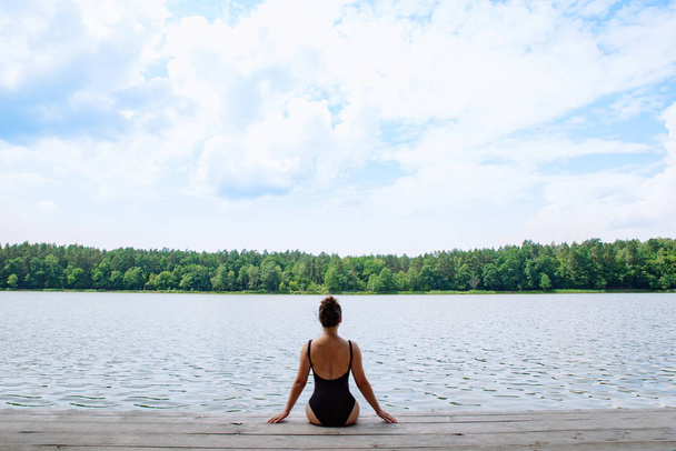 Frau sitzt auf Holzsteg und blickt auf See bei sonnigem Tag - Foto, Bild