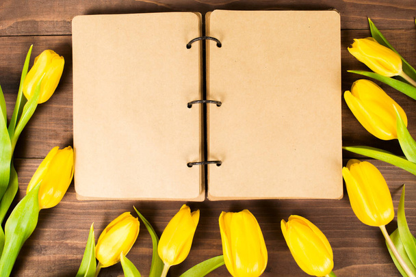 Vintage notebook with copy space on wooden table with yellow tulips, flat lay - Photo, Image