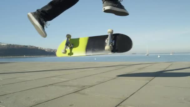 Zeitlupe, Nahaufnahme, dof: unkenntlich gemachte Skateboarder skateboarden und springen 360-Grad-Flip-Trick auf Promenade entlang des Ozeans im sonnigen Sommer. Skateboarder beim Skateboard-Springen Kickflip-Trick - Filmmaterial, Video