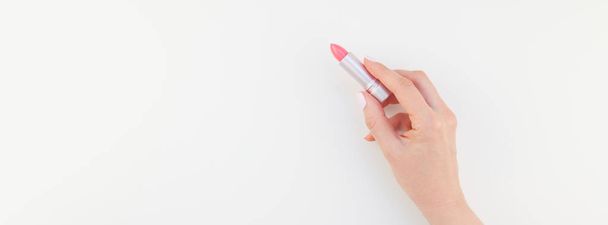 Woman hand with pastel manicure polish holding pink lipstick isolated on white background with copy space. Long wide banner for feminine beauty blog social media - Photo, Image