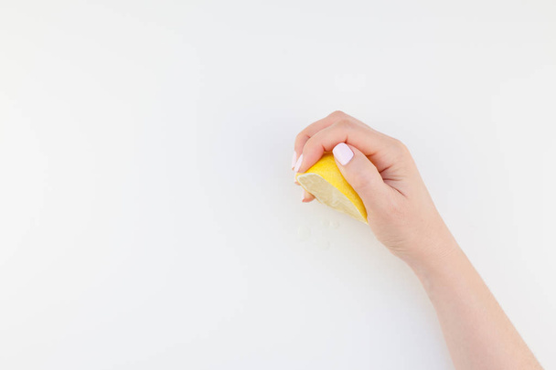 パステル カラーのマニキュア光沢ホワイト バック グラウンド コピー スペース ミニマリズム スタイルに分離されたレモンの半分を保持している女性の手。フェミニンなソーシャル メディアのテンプレートです。健康的な食事の概念 - 写真・画像