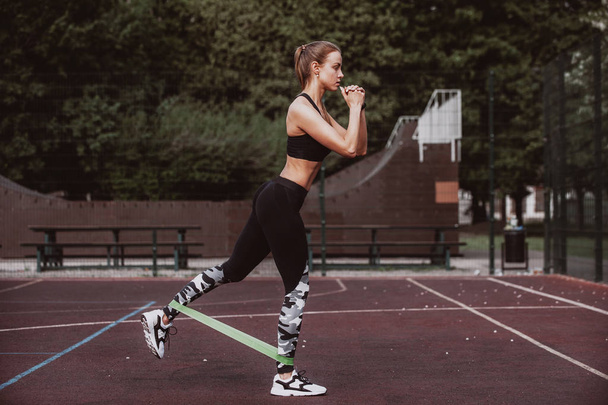 Молодая спортсменка делает упражнения с резиновой лентой на открытом воздухе - Фото, изображение
