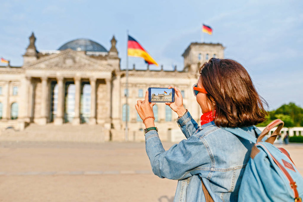 Bella giovane donna in abbigliamento casual scattare foto dal suo telefono cellulare al Bundestag, Berlino
 - Foto, immagini