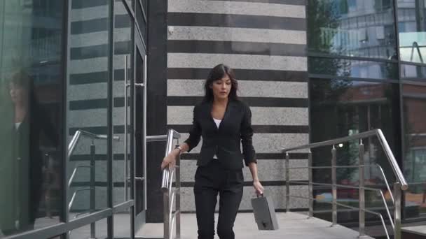 attractive business woman exits from a modern business center and confidently walks down the street - Video, Çekim