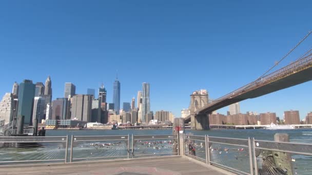VISTA BAJA DEL ÁNGULO: Icónica vista del Puente de Brooklyn y los altos rascacielos contemporáneos del centro de Lower Manhattan desde el muelle del ferry. Puente de Brooklyn que conecta Brooklyn borough y Manhattan en la ciudad de Nueva York
 - Metraje, vídeo