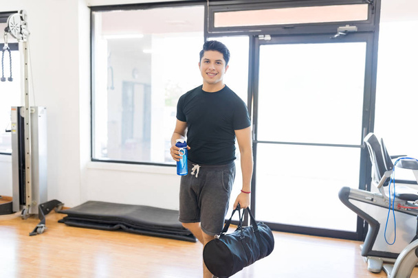 Sorrindo homem apto com garrafa de água e saco de ginástica entrando no health club
 - Foto, Imagem