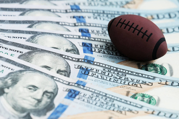 The concept of corruption or sports betting. Souvenir ball for playing rugby or American football on US banknotes. - Fotoğraf, Görsel