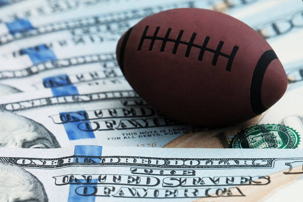 Primo piano di un simbolo di rugby o football americano su uno sfondo di banconote da cento dollari negli Stati Uniti. Il concetto di corruzione o scommesse sportive
. - Foto, immagini