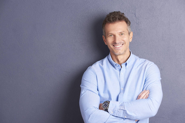Portrait of middle aged businessman wearing shirt and looking at camera while standing at grey background.  - Foto, afbeelding