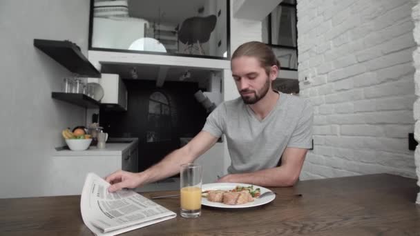 Man Reading Newspaper And Having Breakfast At Home In Kitchen - Materiał filmowy, wideo