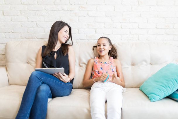 Onnellinen psykologi katselee tyttöä tehdessään muistiinpanoja sohvalla kotona
 - Valokuva, kuva