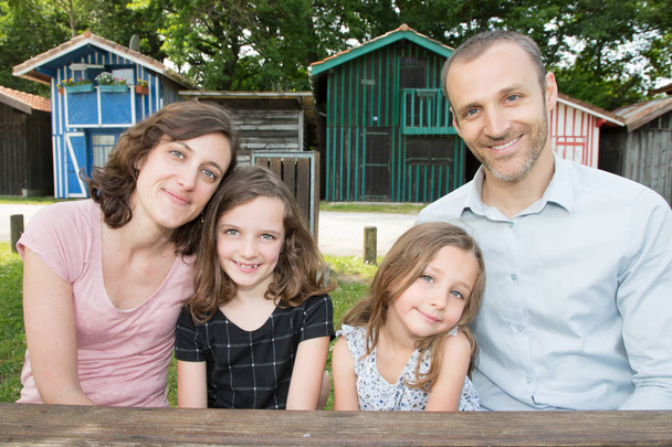 Lächelnde Familie sitzt auf Holztisch im Freien vor Hütte Holzdorf in bassin arcachon in Frankreich - Foto, Bild