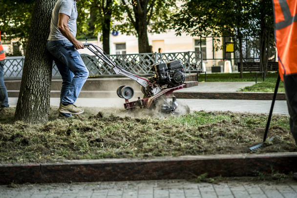 a munkavállalóknak az utcán talaj ápolása traktor géppel növény néhány fát, a város csoport - Fotó, kép