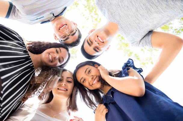 Visão de baixo ângulo do grupo de adolescentes em pé em um aconchego com a cabeça tocando e olhando para a câmera
 - Foto, Imagem