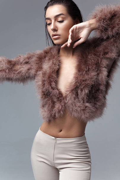 Young elegant girl posing in fluffy pink cape with artificial fur and beige flare trousers on gray background. Fashion retro style - Foto, afbeelding