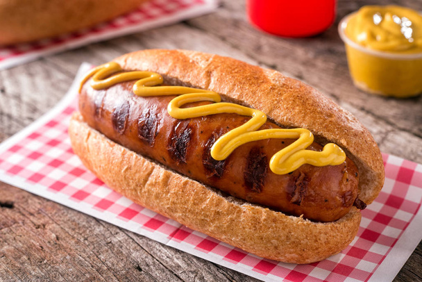 A delicious grilled smoked sausage on a roll with yellow mustard. - Fotoğraf, Görsel