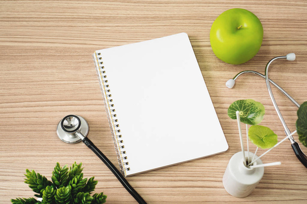 Stethoscope with notebook and apple fruits on wood background. Text copy space. - Photo, Image