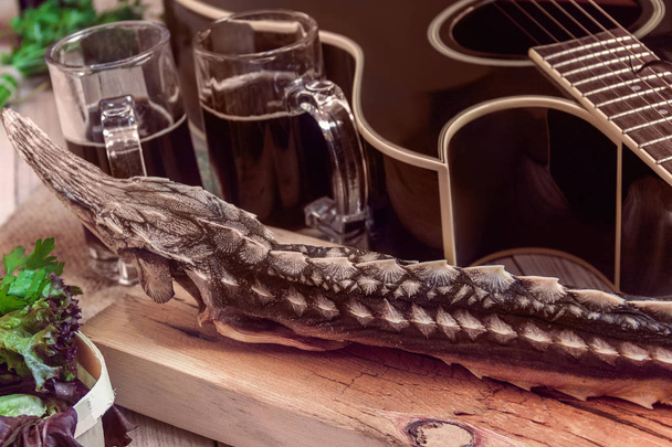 esturión seco con cerveza oscura, verdes y guitarra sobre un fondo de madera
 - Foto, Imagen
