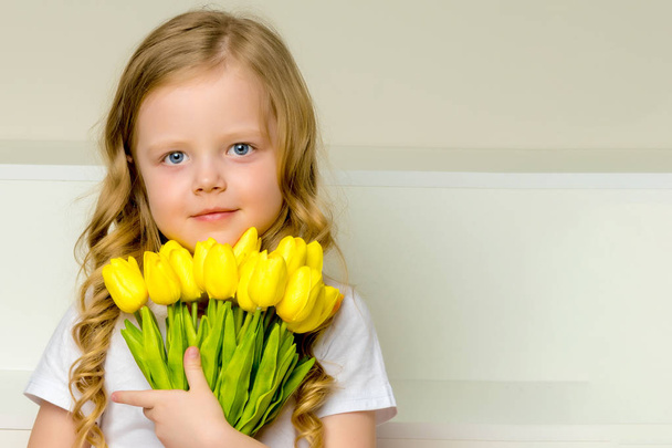 A little girl with a bouquet of tulips is sitting on the stairs. - Foto, Bild