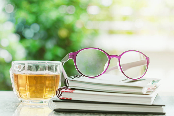 Brýle na kroužkových zápisníků s šálkem čaje rozmazané přírodní zelené pozadí - Fotografie, Obrázek