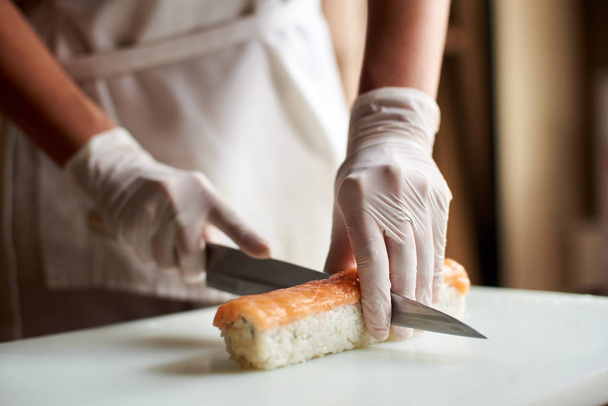 Vista de perto do processo de preparação de sushi de rolamento. Chef está cortando rolo na placa branca
 - Foto, Imagem