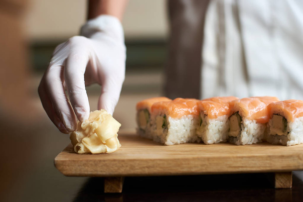 Close-up view of process of preparing delicious rolling sushi. Master's hand is holding ginger - Photo, Image
